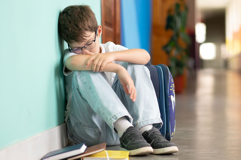 Sad boy sitting alone in a school hallway, showing the impact of bad parenting