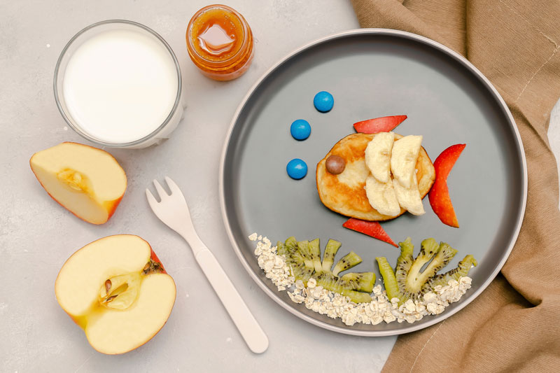 Creative healthy meal for kids with fruit, oats, and pancake shaped like a fish