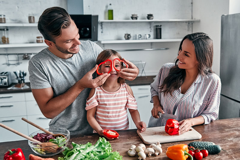 Parents and child cooking together in the kitchen, sharing a joyful bonding moment that reflects positive parenting.