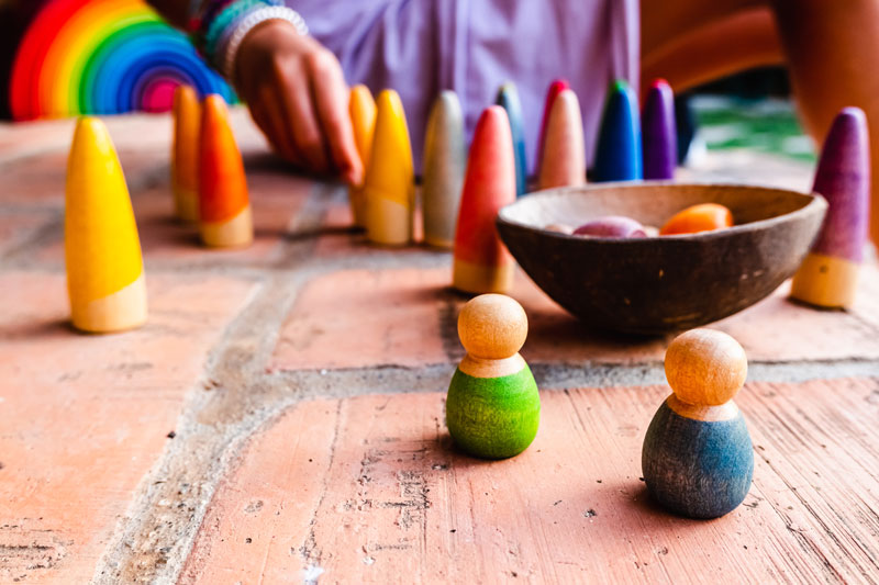Wooden Montessori toys in vibrant colors arranged on a brick floor, with a child playing in the background.