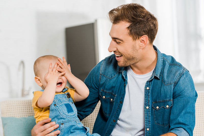 Father playing peekaboo with baby to encourage early language skills