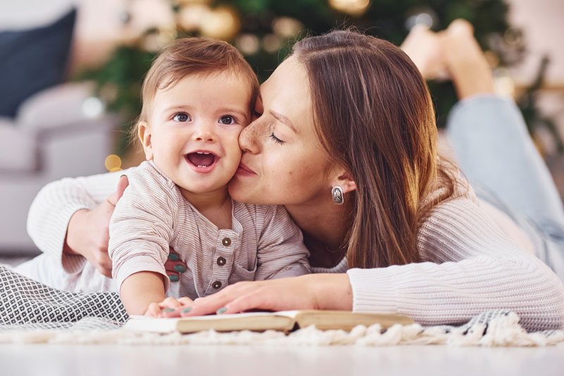 Mother kissing happy baby as loving support during infant milestones month by month