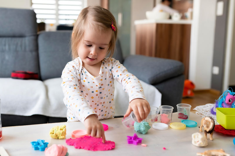 Toddler practicing fine motor activities by playing with colorful clay at home.
